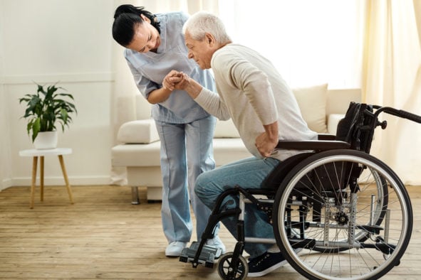 caregiver helping elderly man stand up from wheelchair