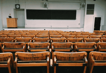 A picture taken from the back of a college auditorium with wooden desks and chairs to illustrate why college is no longer necessary to be successful